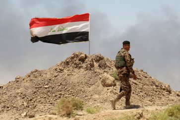 A soldier walks past an Iraqi flag in Husaybah, in Anbar province July 22, 2015. Iraqi security forces and Sunni tribal fighters launched an offensive on Tuesday to dislodge Islamic State militants and secure a supply route in Anbar province, police and tribal sources said. REUTERS/Stringer - GF10000167090